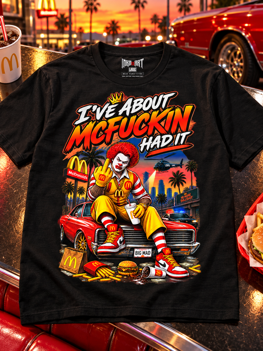 Black McFuckin Had It tee laid front-up on dark diner tabletop with red and warm yellow reflections, with the INKDnART interior neck tag.