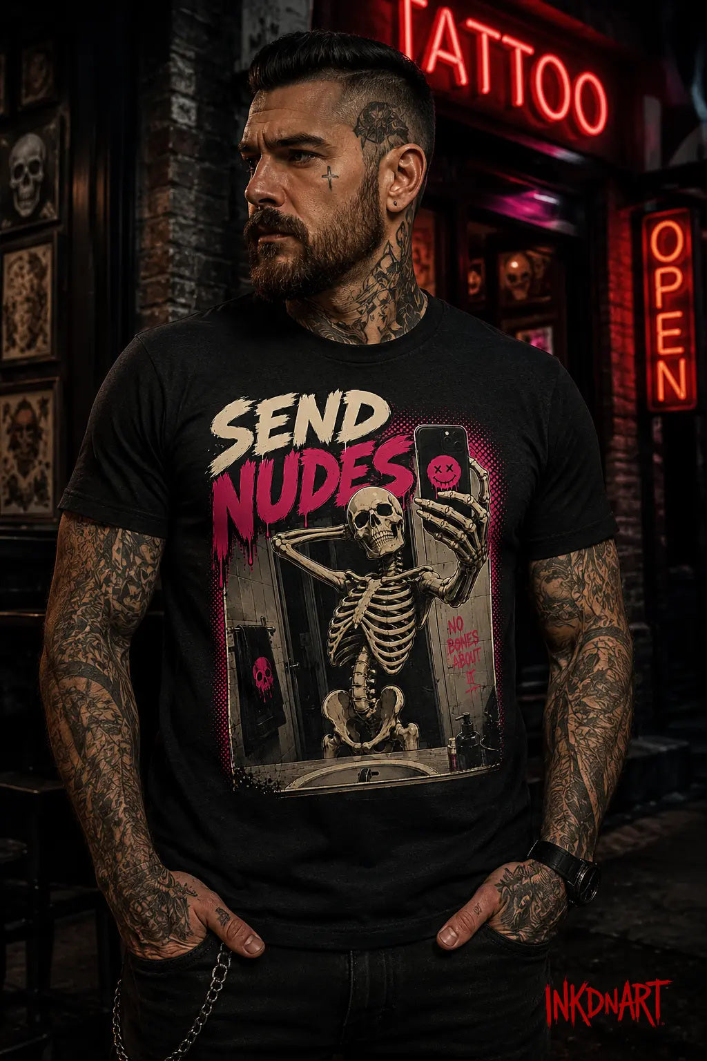 Send Nudes Tee – skeleton selfie graphic tee in bone and hot pink, worn by model outside a tattoo shop at night
